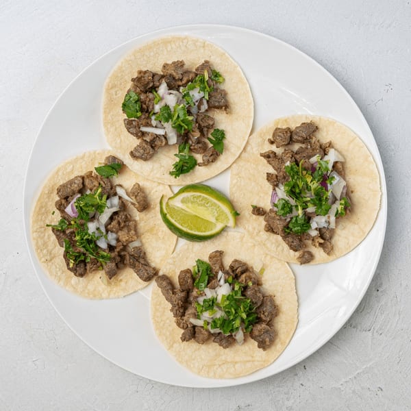 Four Muchas Gracias Mexican Food street tacos with carne asada, cilantro, onions, and a lime wedge.