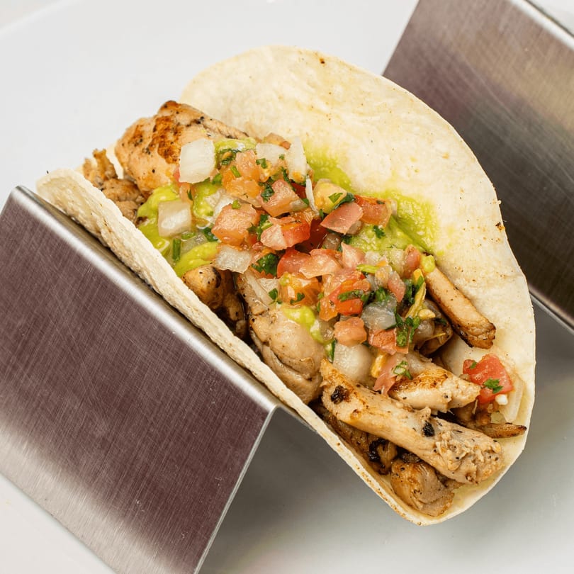 Muchas Gracias Mexican Food chicken taco with guacamole and pico de gallo in a metal holder.