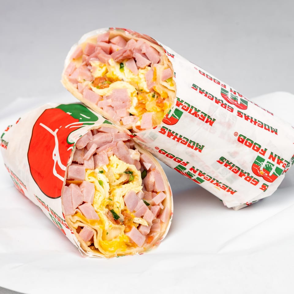Two Muchas Gracias Mexican Food breakfast burritos, cut in half, revealing ham, eggs, and cheese.