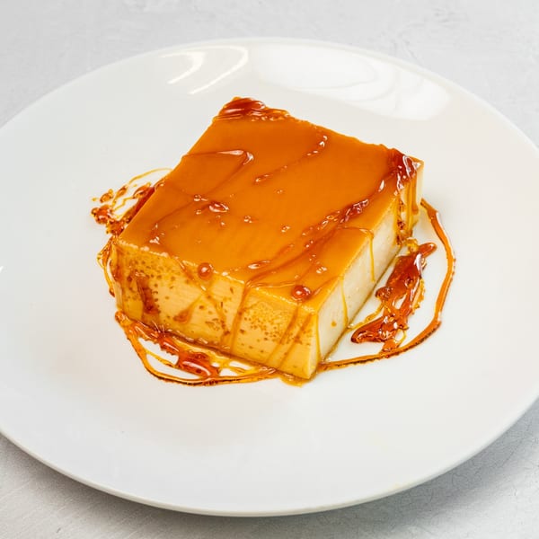Muchas Gracias Mexican Food's flan dessert, a rectangular custard with golden caramel sauce on a white plate.